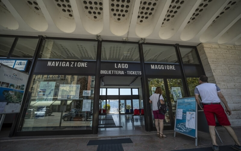 Entrance of a ticketing center with glass facade, double doors, and a man and woman in casual attire standing outside.