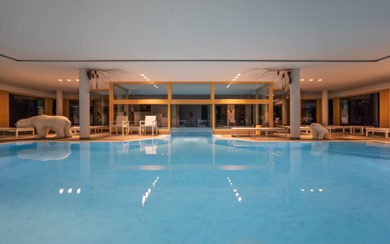 Indoor pool scene with light blue water, white polar bear statues, and a seating area, illuminated by natural light.