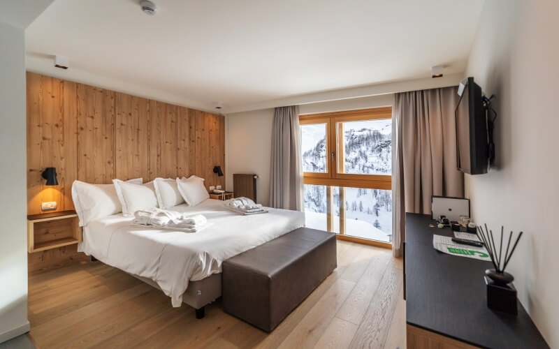 Serene hotel room with white decor, comfortable bed, desk, and mountain view through a large window.