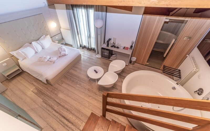 Modern hotel room featuring a bed, bathroom with a tub, and a seating area, all in a minimalist design with natural light.