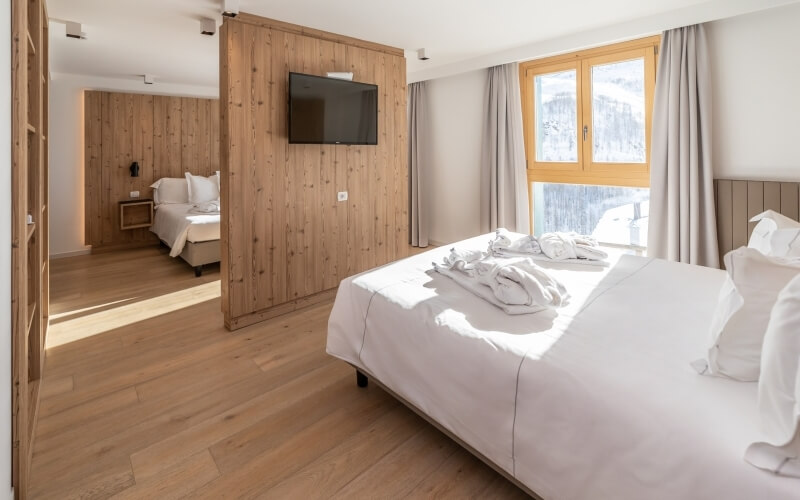 Hotel room with two beds, a TV, and a snowy outdoor view through an open door and window with curtains.