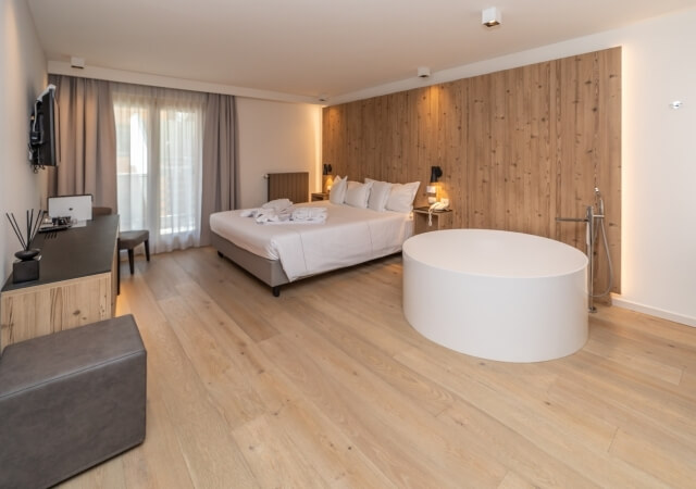 Modern minimalist bedroom with a white bed, circular bathtub, large window, and natural light from sheer curtains.