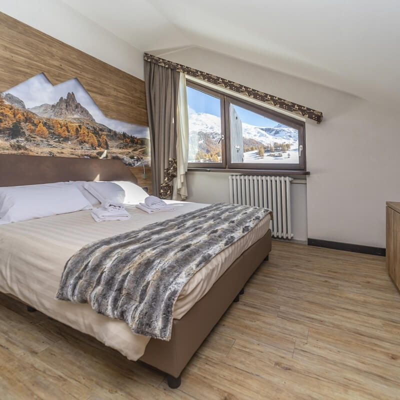 Cozy bedroom with a large bed, mountain print headboard, window view of snow-capped mountains, and warm wooden accents.