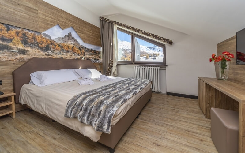 Serene bedroom with a king-size bed, wooden desk, red flowers, mountain view, and a nature mural.