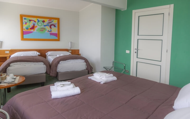 Camera d'hotel con due letti, biancheria bianca, coperte marroni, dipinto colorato e atmosfera rilassante.