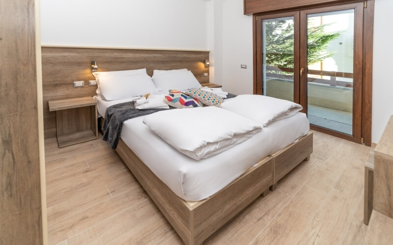 Cozy bedroom with a bed, nightstand, and sliding glass doors, featuring white decor and a serene outdoor view.