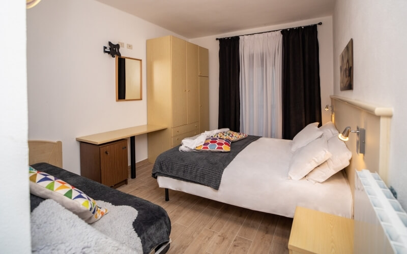 Camera d'hotel con due letti, armadio beige, scrivania e specchio, decorata in toni chiari e atmosfera serena.
