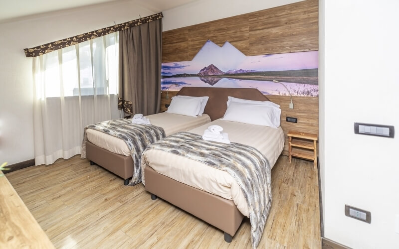 Serene hotel room with two beds, wooden floor, scenic mural, natural light, and modern amenities for guest comfort.