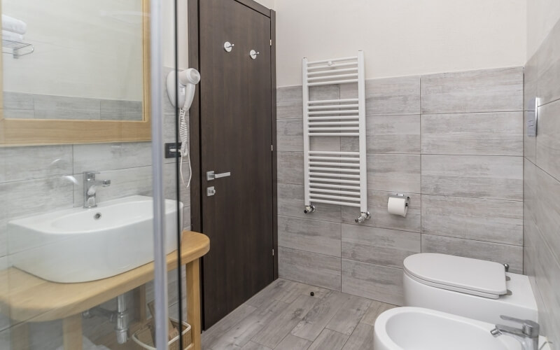 Bathroom with sink, toilet, and bathtub; white walls, gray tile floor, dark brown door, and wall-mounted hair dryer.