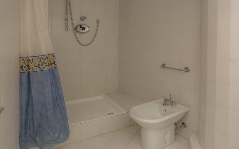 Bathroom featuring a blue and white floral curtain, white bathtub, silver showerhead, and small sink with a towel rack.