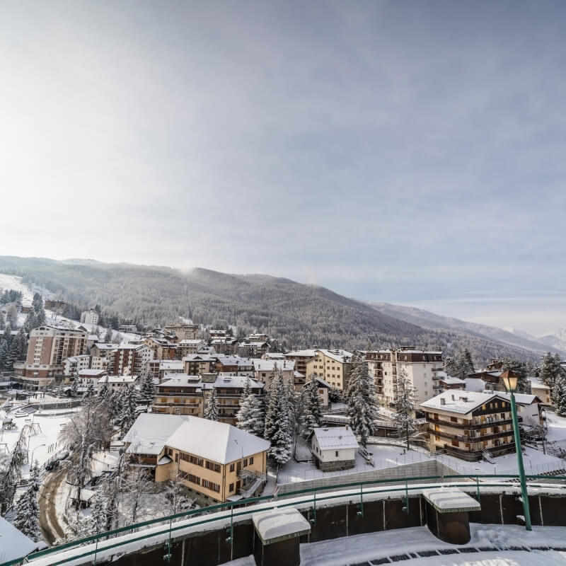 Città innevata in una valle, con montagne sullo sfondo e un impianto di risalita, atmosfera serena invernale.