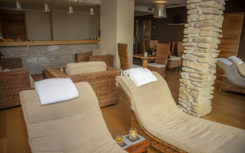 Area di attesa interna con poltrone, tavolino con candele e parete in pietra, creando un'atmosfera rilassante.