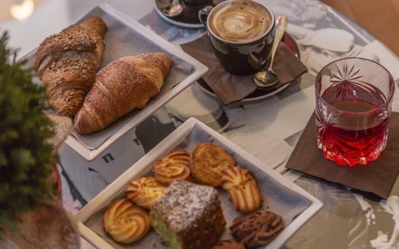 A cozy table setting with croissants, a glass of red drink, and a cup of coffee on a marble-patterned tablecloth.