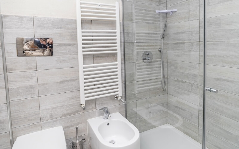 Modern bathroom featuring a toilet, bidet, shower, light wood grain tiles, and a selfie picture above the toilet.