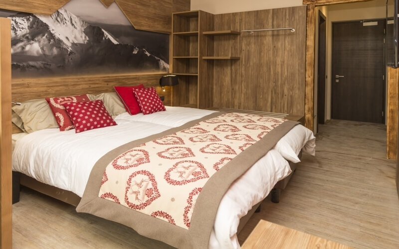 Cozy bedroom with a large bed, mountain photograph, wooden shelving, and light wood floor, creating a serene atmosphere.