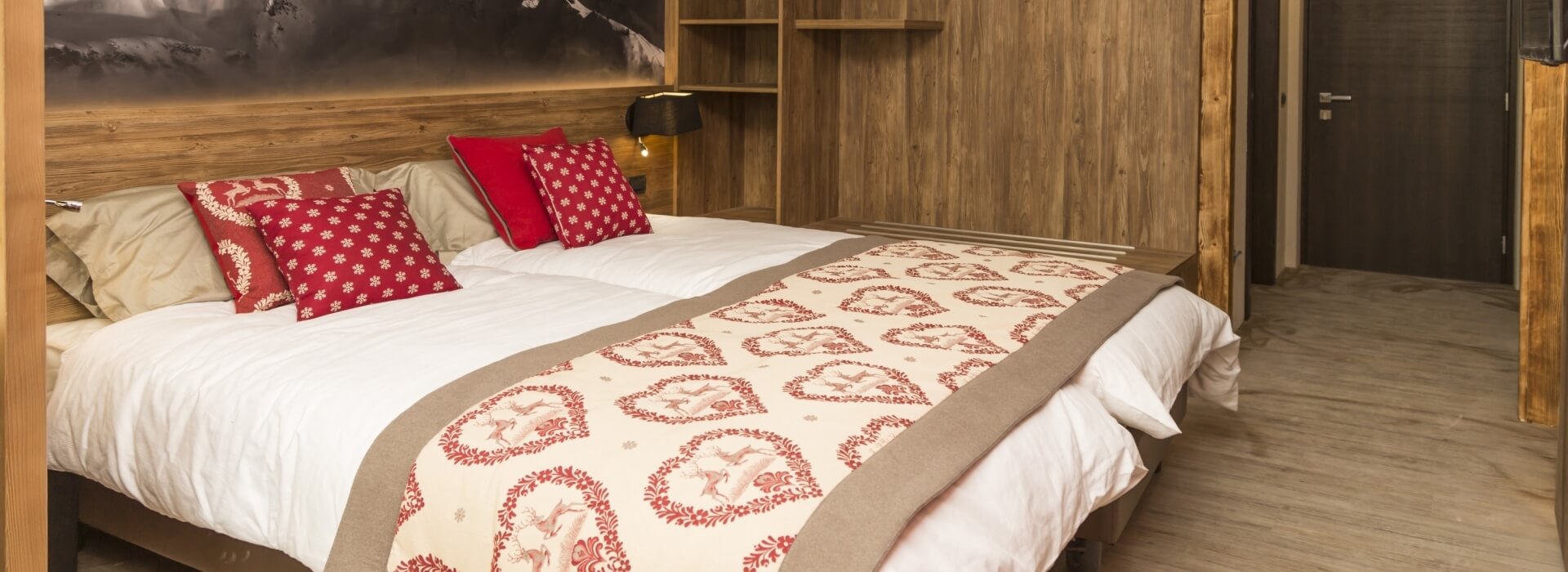 Serene bedroom with a white and red patterned comforter, wooden headboard, and light-colored wooden floor, evoking tranquility and coziness.