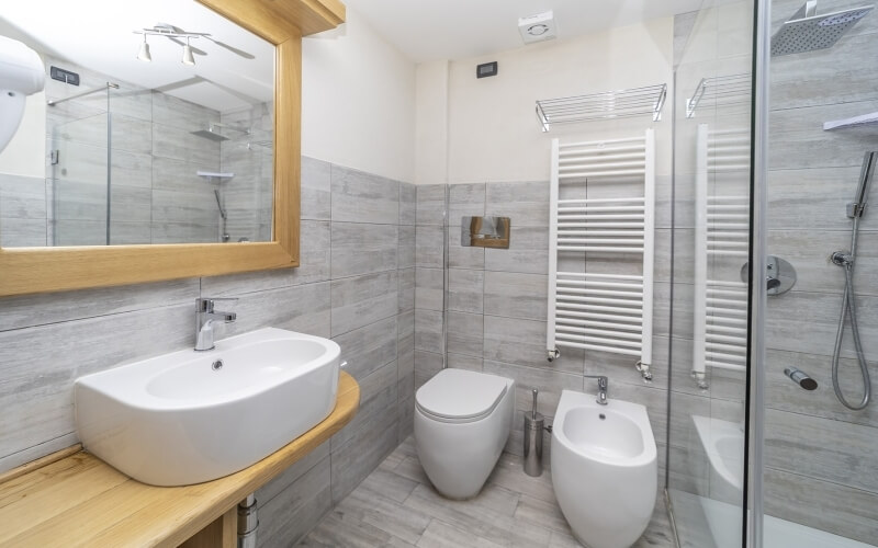 Cozy bathroom featuring a wooden vanity, bidet, toilet, and a glass-walled shower stall with natural lighting.