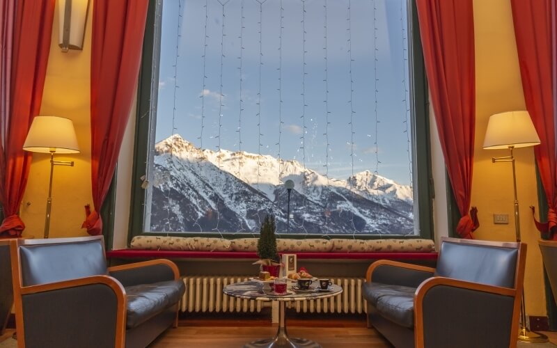 Cozy seating area with a window view of snow-capped mountains, adorned with colorful curtains and tea-time essentials.