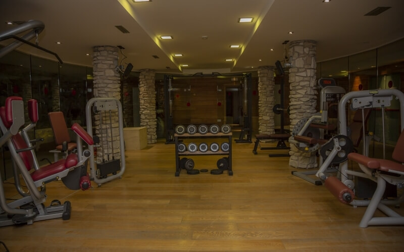 A modern gym with exercise machines, weights, glass walls, and a mirrored background, featuring a clean, organized layout.