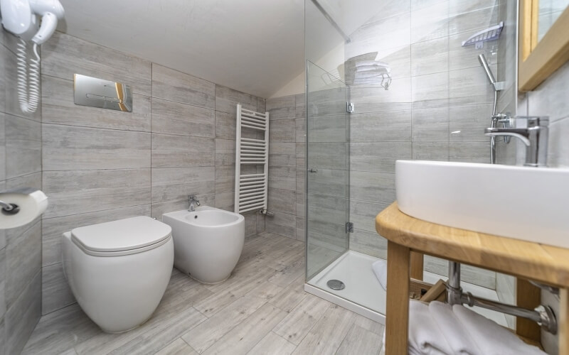 Modern bathroom with shower, sink, toilet, gray wood-look tiles, and functional fixtures including a towel rail and heater.