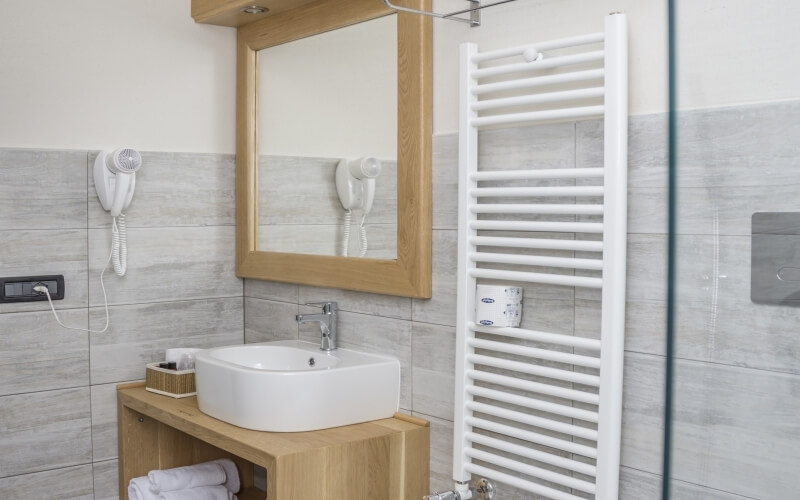 Modern bathroom featuring a white sink, mirror, towel rack, hair dryer, toiletries, and a glass door.