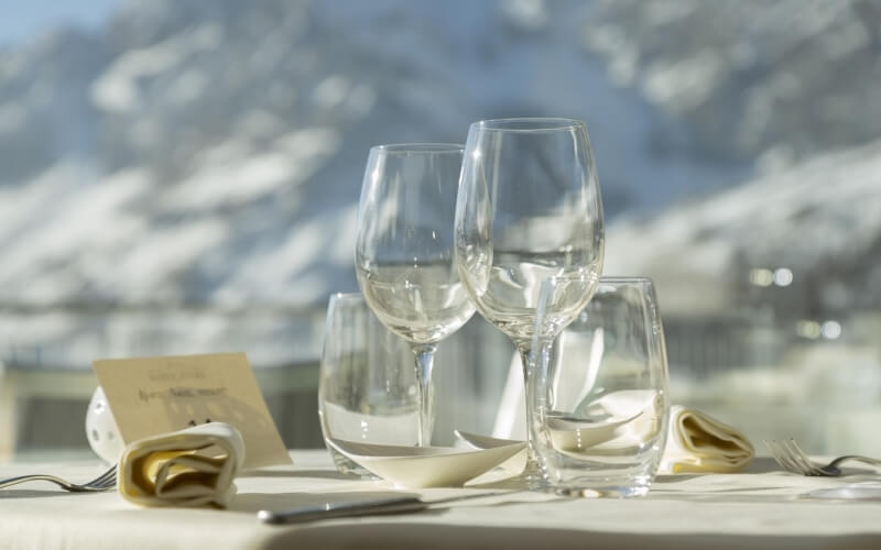 Table setting with four wine glasses in a pyramid, two forks, two napkins, and a white card, against a snowy mountain backdrop.