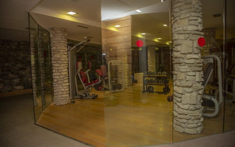 Interno moderno di una palestra con parete di vetro, colonna di pietra e attrezzature per il fitness ben disposte.