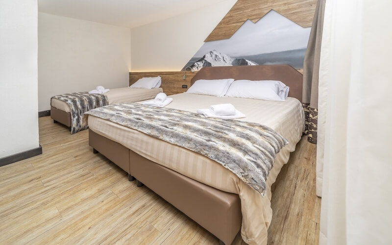 A cozy room with two beds, white bedding, a brown headboard, and a mural of snowy mountains behind them.