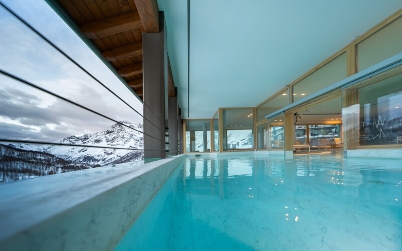 Modern minimalist swimming pool with mountain view, high ceiling, and abundant natural light in a serene setting.