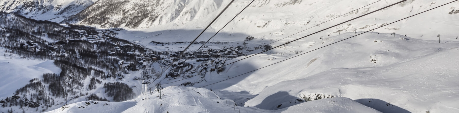 Serene winter landscape with snow-covered mountains, a village among trees, and a ski lift system in the foreground.