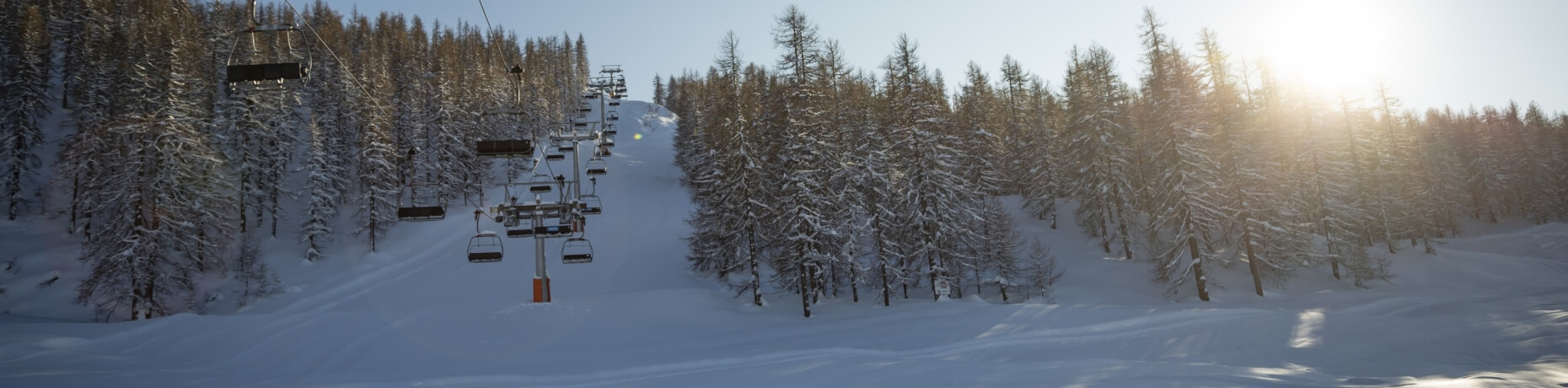 Serene winter scene with a ski lift, snowy landscape, bright blue sky, and evergreen trees surrounding a frozen lake.