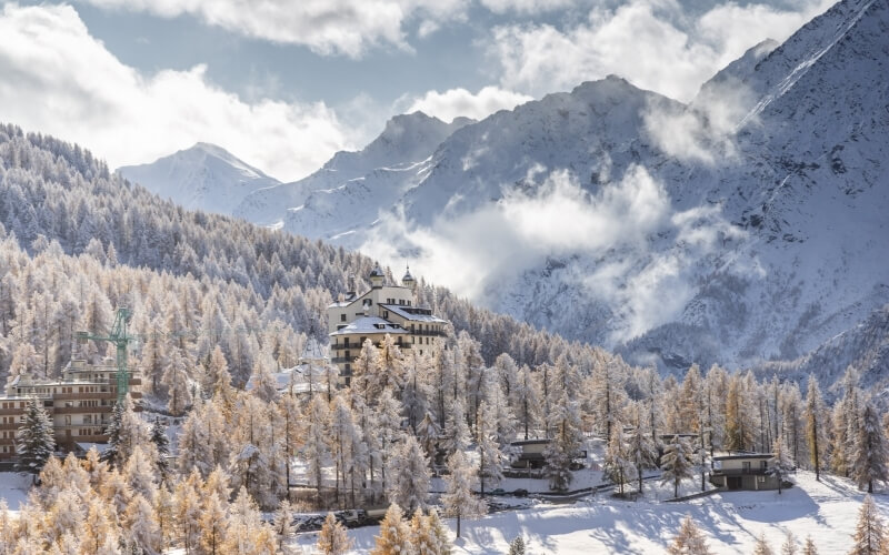 Serene winter landscape with snow-covered mountains, a cozy village, and frosty trees under a mostly cloudy sky.