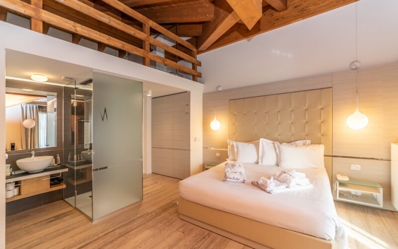 Modern hotel room with a large bed, elegant bathroom, loft area, and light hardwood floors, exuding luxury and comfort.