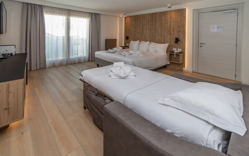 Spacious minimalist bedroom with three gray fabric beds, hardwood floor, large windows, and modern decor in neutral tones.