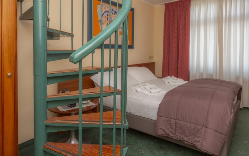 Cozy bedroom with a spiral staircase, bed with brown comforter, red curtains, and green carpet, exuding warmth.