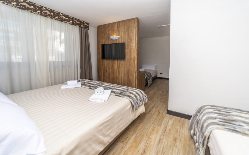 Hotel room with two beds, white sheets, wood paneling, light wood floor, and a mounted TV, exuding simplicity and elegance.