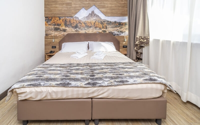 Serene bedroom with a bed, mountain mural, wooden panel, sheer curtains, and light wood floor, creating a peaceful atmosphere.