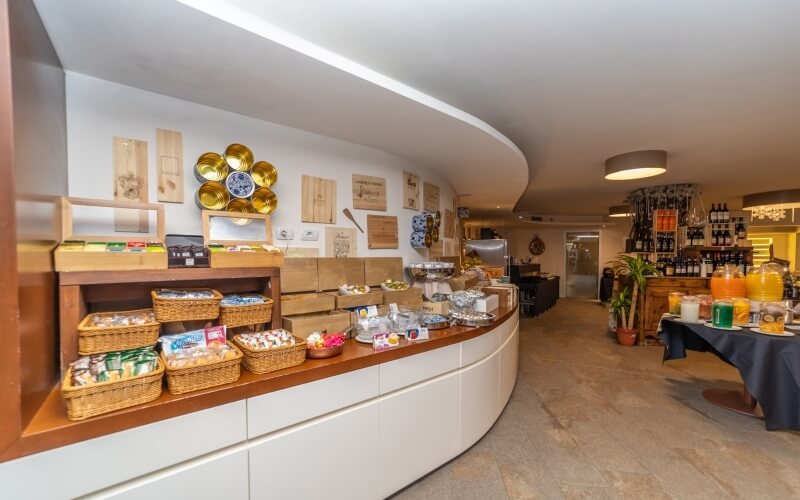 Modern curved buffet counter with food baskets, wooden decor, beverage table, wine wall, and bright welcoming atmosphere.