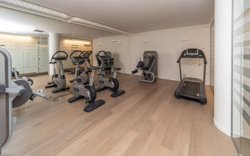 A compact, well-lit gym with exercise equipment, mirrored wall, and light wood floor, creating a clean, modern atmosphere.