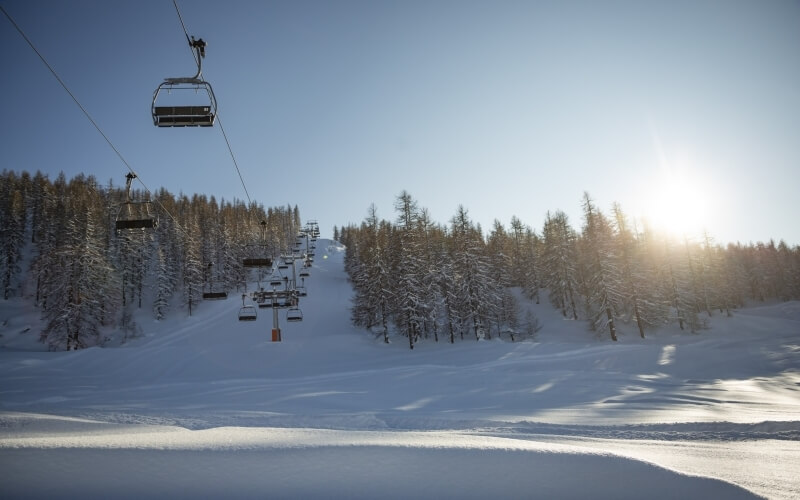 Ski lift descending a snow-covered mountain, surrounded by a snowy forest and bright sunlight under a clear blue sky.