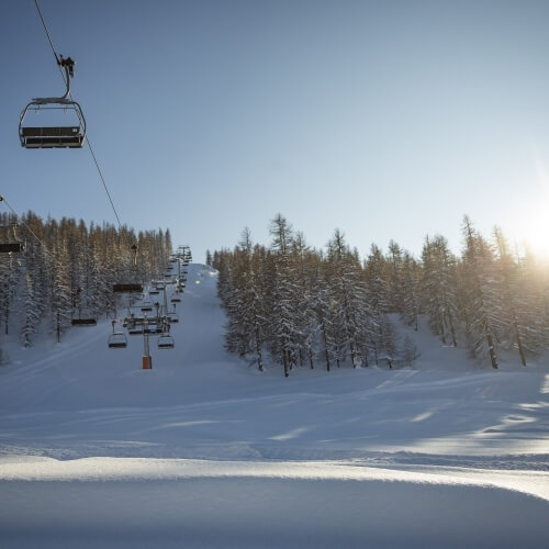 Serene winter scene with a ski lift, snow-covered slope, glistening powder, and trees under a clear blue sky.