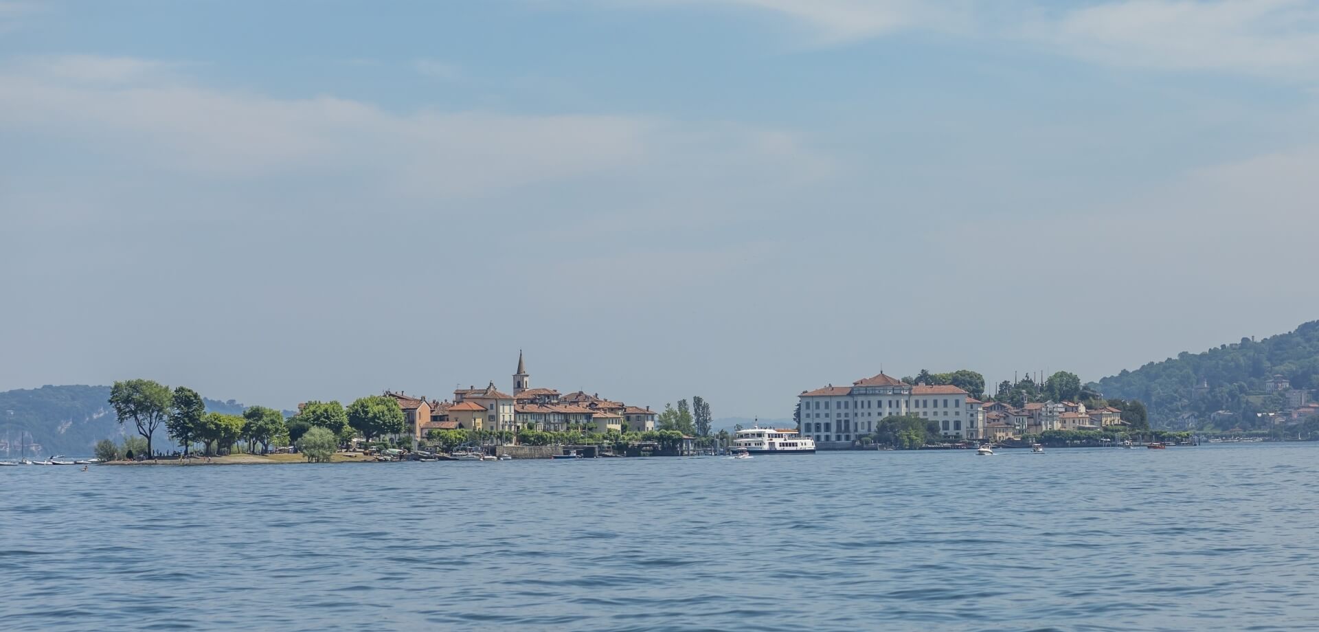 Serene scene of calm dark blue water with a distant lush island featuring white buildings and a soft blue sky.