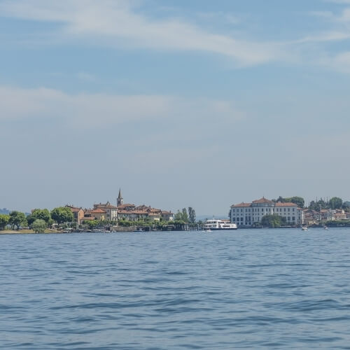 Serene landscape featuring light blue water, distant shoreline with buildings and trees, under a blue sky with white clouds.