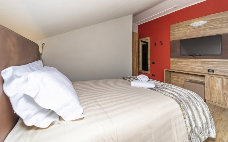 Camera d'albergo con letto grande, TV, bagno visibile, decorazioni in toni neutri con tocchi di rosso.