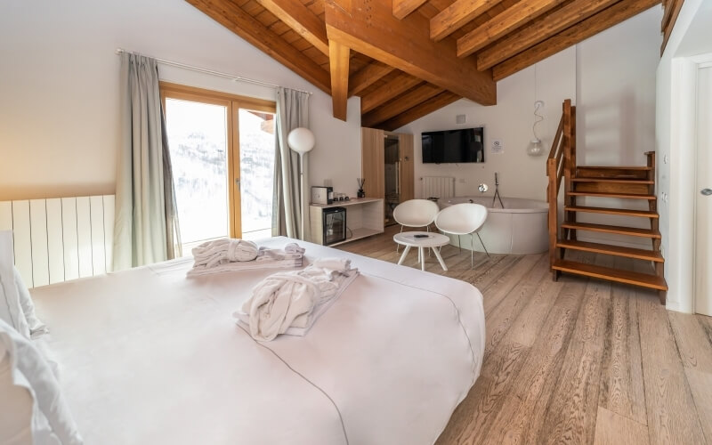 Elegant hotel room with a white color scheme, double bed, freestanding bathtub, and wooden staircase, exuding luxury and comfort.