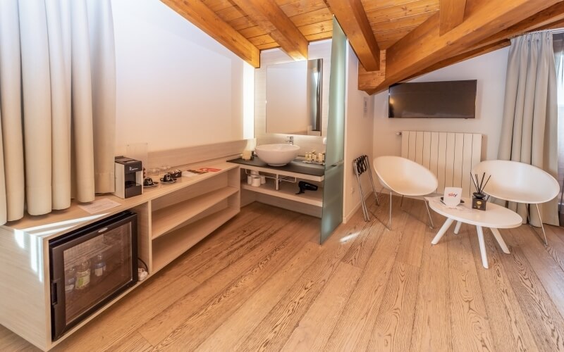 Modern small room with kitchenette, sitting area, natural light, wooden ceiling, and cozy decor.