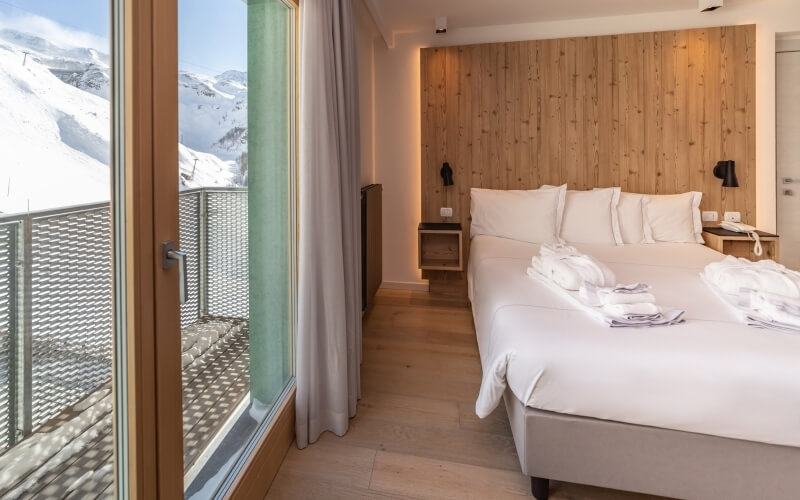 Serene hotel room with two beds, wooden decor, and a balcony showcasing stunning snow-capped mountain views.