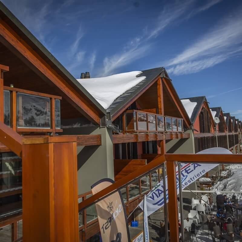 Modern multi-level building with wood and glass exterior, snow-covered roof, and serene blue sky in the background.