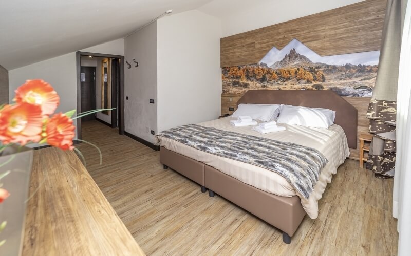 Serene bedroom with a brown leather headboard, white comforter, landscape mural, and colorful flower arrangement.