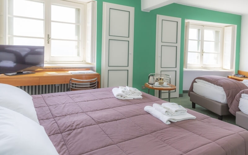 Cozy hotel room with two beds, one pink and one brown, a TV, window, and a small table with a kettle and cups.